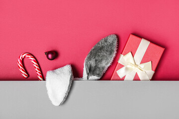 Bunny ears with Christmas ball, gift and candy cane on color background