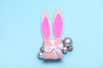 Paper bunny ears with Christmas balls and gift on blue background
