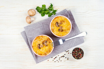 Chicken and mushroom casserole with golden crust, julienne with baked cheese, creamy gratin in portion ramekin clay pot on white wooden background. French cuisine. Top view, flat lay with copy space
