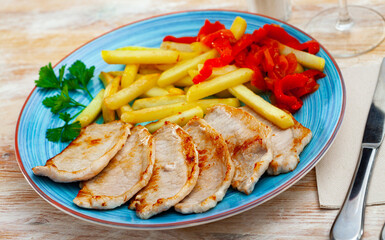Juicy pork fillet steaks with vegetable garnish of fried potatoes, baked red bell pepper and fresh greens..