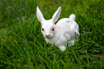 White ceramic figurine of rabbit in the green grass. Symbol of 2023 year