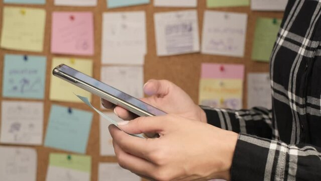 Using a smartphone for planning tasks and calendar events in the office, use of digital technologies to change a business model. Sticky notes on a cork board in the background. Selective focus