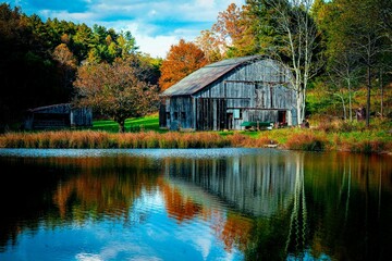 Old wooden barn near a tranquil lake surrounded by beautiful autumn trees