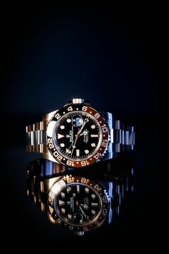 Vertical shot of rosegold Rolex on reflective surface on black background