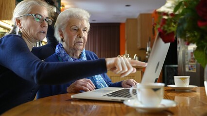 Mature woman helps elderly woman mother with laptop computer.