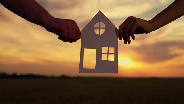 Dream to buy house. Symbol of house, happiness. Home for children and parents, Familys hands are holding paper house at sunset, sun is shining through window. Concept of building house for family.
