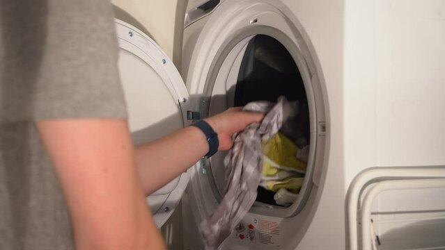Young man loads clothes into white laundry dryer, then closes door