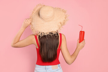Young woman in straw hat holding tin can with beverage on pink background, back view