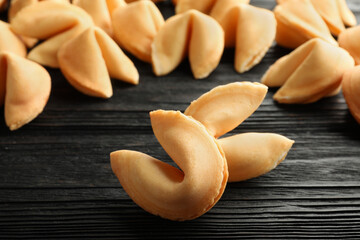 Fototapeta na wymiar Tasty fortune cookies with predictions on black wooden table, closeup