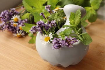 Mortar with fresh lavender, chamomile flowers, herbs and pestle on wooden table