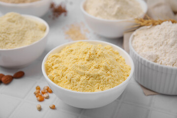 Bowls with different types of flour on tiled table, closeup