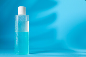 Wet bottle of micellar water on light blue background, space for text
