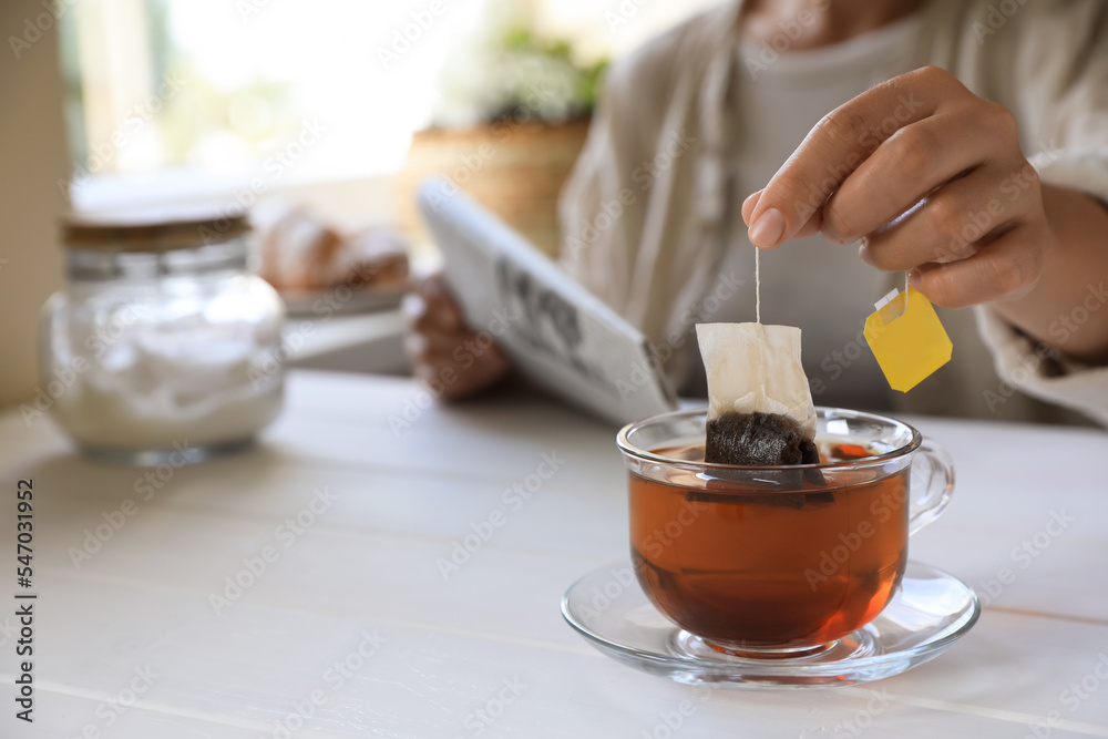 Poster Woman taking tea bag out of cup at white wooden table indoors, closeup. Space for text