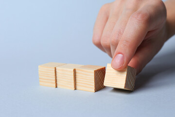 Woman arranging cubes on light background, closeup. Idea concept