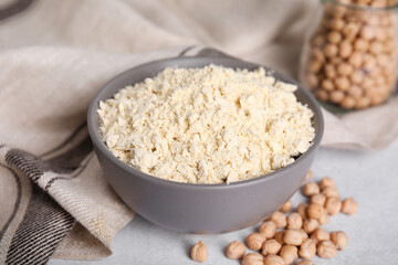 Chickpea flour in bowl and seeds on light grey table, closeup