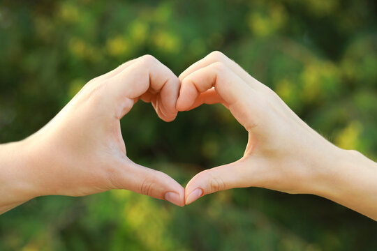 Couple making heart with hands outdoors on sunny day, closeup
