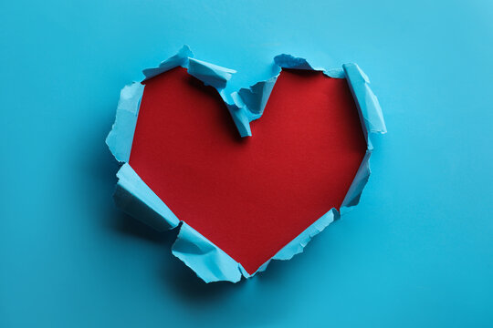 Torn heart shaped hole in light blue paper on red background