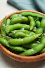 Bowl of green edamame beans in pods with salt on light grey table, closeup