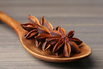 Spoon with aromatic anise stars on wooden table, closeup