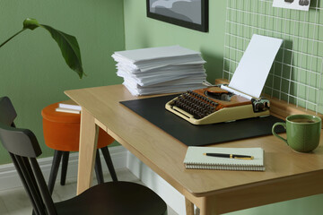 Typewriter, stack of papers and mood board on wooden table near pale green wall. Writer's workplace
