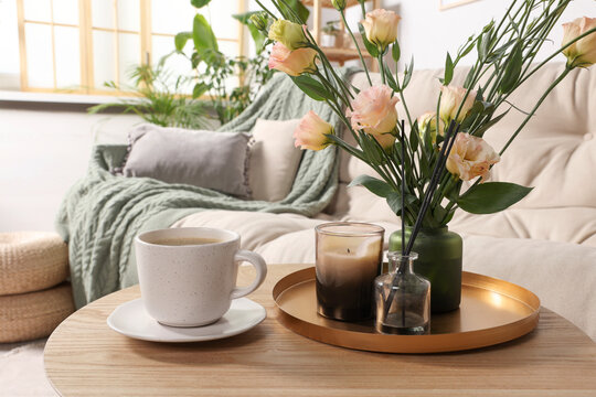 Beautiful flowers and cup of drink on wooden coffee table in living room