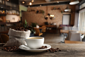 Cup of hot aromatic coffee and roasted beans on wooden table in cafe, space for text