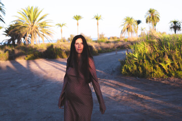 young pregnant woman relaxes in the golden light of sunset in a green natural place of plants and palm trees