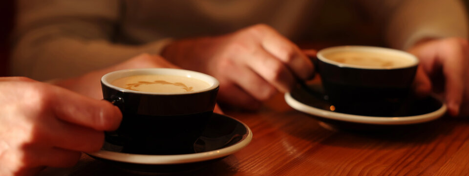 People with cups of aromatic coffee at wooden table, closeup. Banner design