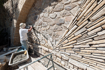 Stone mason installing hand cut stone in a radial pattern on an existing rock wall - obrazy, fototapety, plakaty