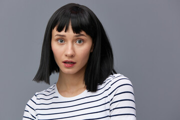 a sweet, attractive, surprised woman stands on a gray background in a white striped T-shirt and looks at the camera with her eyes wide open. Horizontal photo