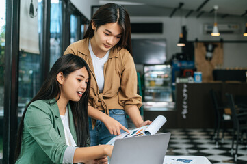 Young woman and female colleague working on laptop computer in coffee shop