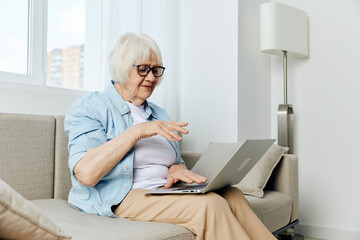 a nice retired woman sits at home and uses a laptop holding it on her lap sitting on the couch typing text working from home