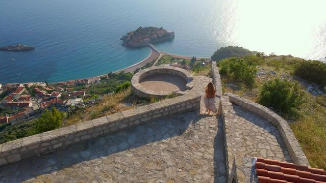 Young woman visits the Saint Sava church which is located above the Sveti Stefan island near the city of Budva. She is running to the view point. Travel to Montenegro concept. Slowmotion aerial video