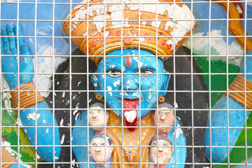 Hindu Goddess Kali with her tongue hanging out behind the bars on the wall of the temple. India.