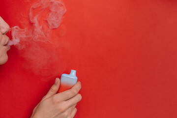 Inhalation of smoke from vape in female hand against red background.