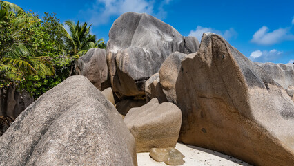 Enorme granieten rotsblokken op een tropisch eiland. Detailopname. Mooie vorm, gladde golvende hellingen. Weelderige vegetatie rondom. Blauwe lucht, wolken. Seychellen. La Digue. Anse Source D& 39 Argent-strand