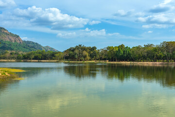 Beautiful and peaceful view of large reservoir with surrounding mountain and trees in beautiful sunshine and cloudy sky in Thailand. Tranquil and beautiful natural scenery landscape of reservoir lake.