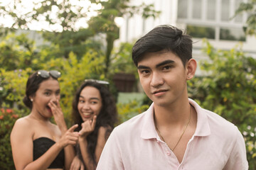 Obraz premium A young man is aware of the attention he gets from two young women giggling in excitement behind him. Feeling handsome and confident. Outdoor scene,