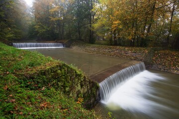 Two weirs on a river in a foggy autumn morning. Juhyn. Moravia. Czechia.