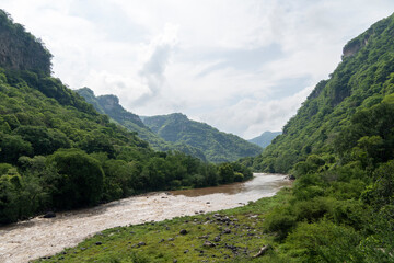 Fototapeta na wymiar dirty river seen through the huentitan ravine in guadalajara, green vegetation, trees, plants and mountains, mexico