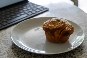 pancake or cupcake on ceramic plate, terrazzo table, tablet in the back. Enjoying sweet bread while working