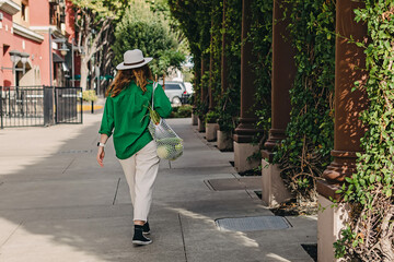 Woman in green jacket walking on the street with a bag of vegetables