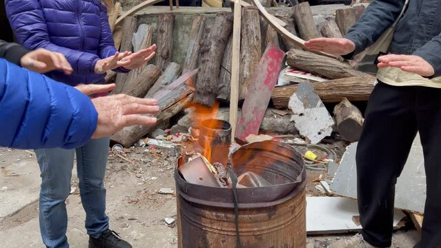 Group of homeless people getting hands warm around fire large rusty barrel on street. Winter season cold weather challenges concept