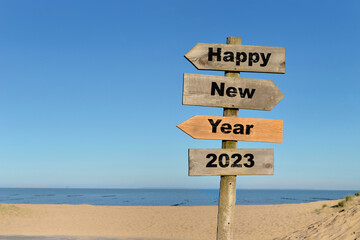 2023 happy new year written on a direction sign in front of a beach on blue sky
