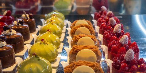 Row of mini cakes covered with pistachio cream, chocolate and fresh raspberry fruit