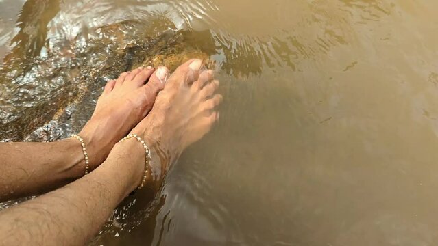 feet of a woman with anklets being washed by flowing water in a river stream 