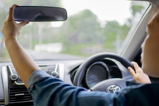 Young woman adjusting the rearview mirror in her car. Ensuring she has a clear view of her surroundings.