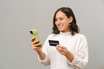 Portrait of young woman using mobile phone and buying online with credit card over grey background