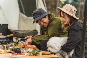 秋冬のキャンプ場で犬と一緒に料理を作るカップルキャンパー
