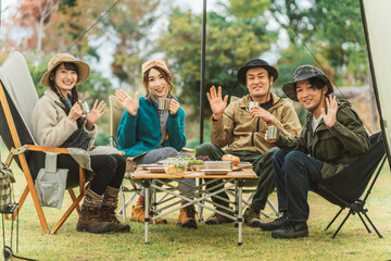 秋冬のキャンプ場で仲間と一緒にコーヒーを飲むアジア人男女
